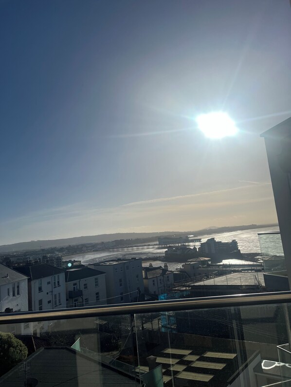 A view from a balcony overlooking a coastal cityscape with buildings, a pier, and a body of water.