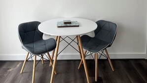 Un coin repas avec une table ronde et deux chaises, un tableau représentant une scène de plage et un thermostat fixé au mur.
