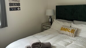 Un lit bien fait, avec une serviette pliée, une lampe de chevet et un oreiller orné du mot « SMILE ».
