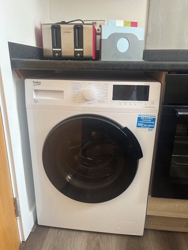 Een voorlader wasmachine met een digitaal scherm, een bedieningspaneel en een sticker met de tekst 'REGISTER NU'.
