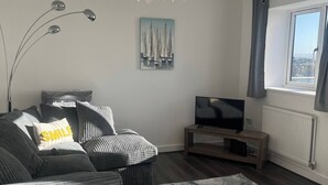 Un salon moderne avec un canapé, un téléviseur posé sur un meuble en bois, un tableau accroché au mur et une vue par la fenêtre.