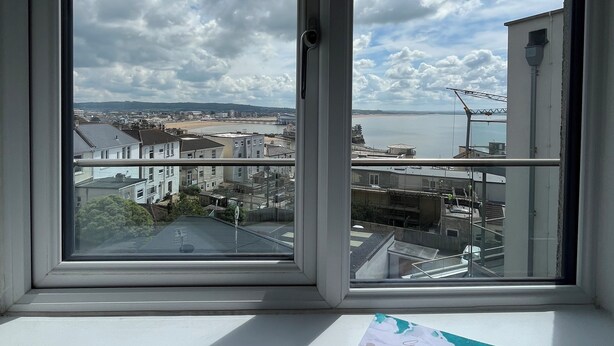 Une fenêtre donnant sur un paysage urbain, un carnet et un stylo posés sur une table.