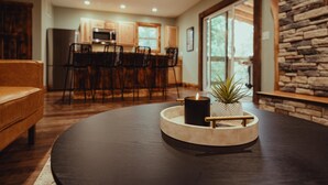 A modern living room with a dark round table, a leather sofa, and a kitchen in the background.