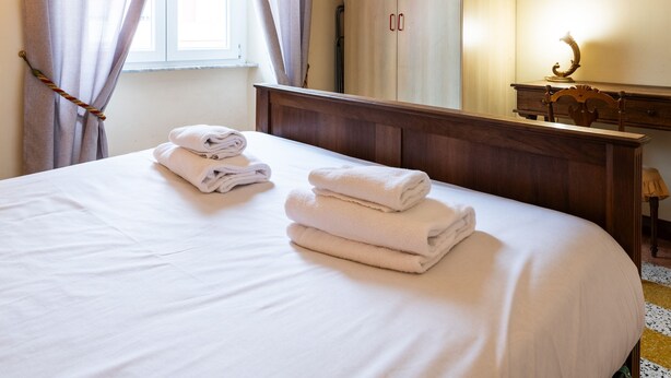 Une chambre d’hôtel avec un lit, une commode en bois, un miroir et une fenêtre avec des rideaux.
