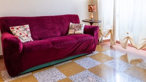 Une pièce avec un canapé en velours rouge, un tableau encadré au mur, une petite table avec une lampe et un sol à carreaux.
