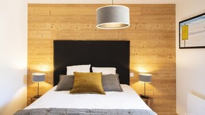 A bedroom with a wooden wall, a black headboard, a grey pendant lamp, and a framed picture on the wall.
