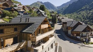 A mountain village with wooden houses, a clear road, and snow-capped mountains in the background.