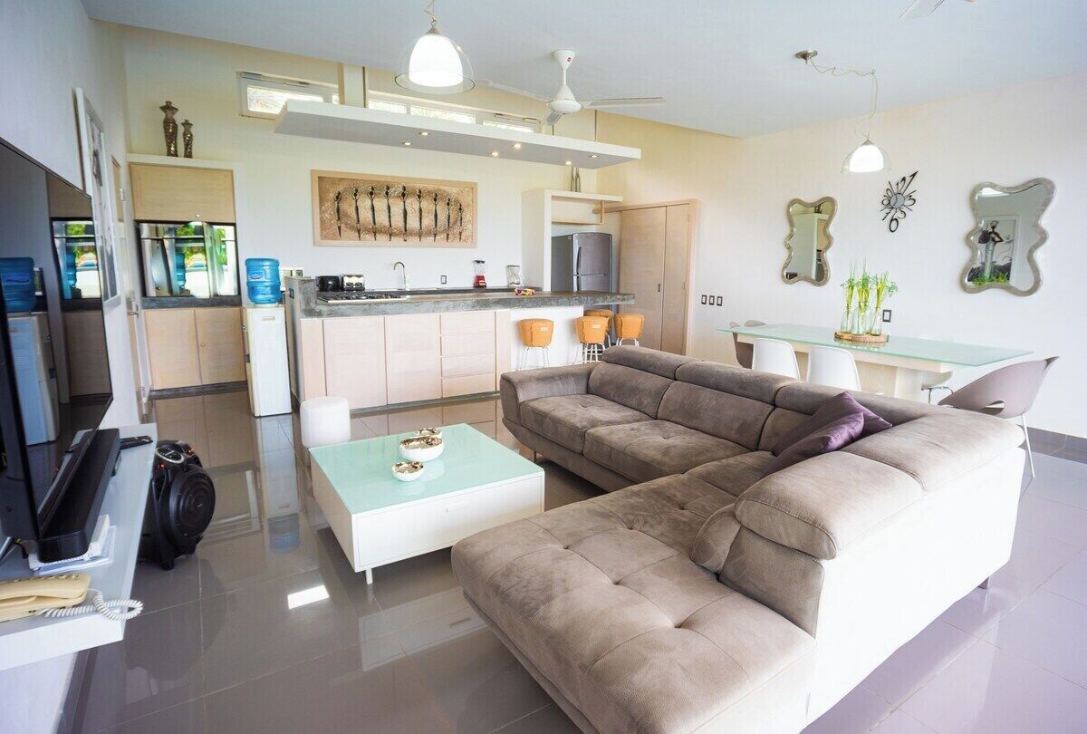Een moderne keuken met een centraal eiland, een eetgedeelte met een glazen tafel en een zithoek met een grote bank.