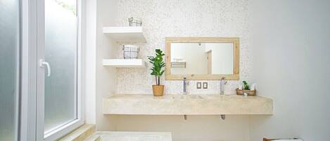 A bathroom with a large window, a sink with a mirror, shelves, and a bench.