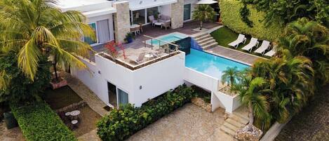 Una casa moderna con piscina, mobiliario exterior y abundante vegetación.