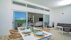 A dining area with a white table set for six, surrounded by wicker chairs.
