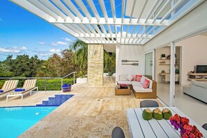 A modern outdoor living area with a pool, lounge chairs, a seating area with a sofa, and a pergola providing shade. - V02b Las Palmas · Villa on the Edge of the Hill (Cabarete)