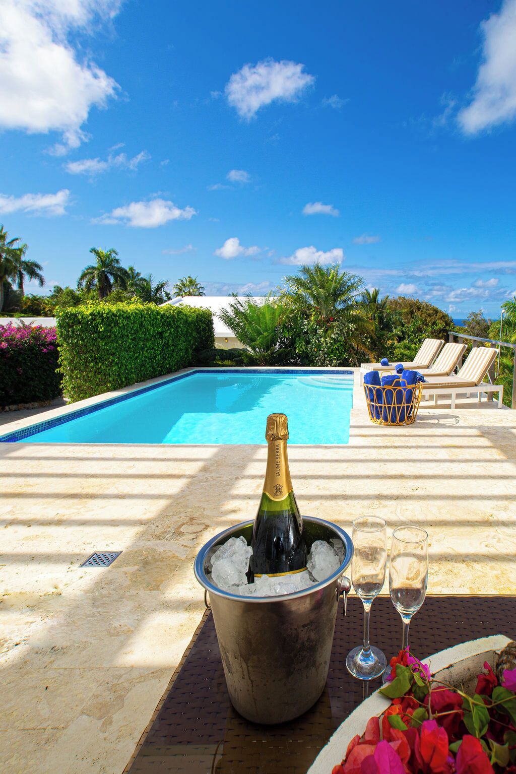 A poolside setting with a bottle of champagne in an ice bucket, a glass, and a flower arrangement.