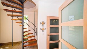 Eine Wendeltreppe mit Holzhäuschen und Metallgeländern, die zu einem Raum mit einer Holztür und rauen Glasscheiben führt.