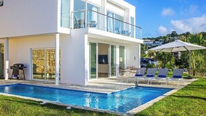 Ein modernes, zweistöckiges Haus mit Swimmingpool, Sitzgelegenheiten im Freien und Grillplatz.