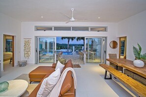 Una sala de estar moderna con un sofá, una mesa de comedor de madera y vistas a una piscina y zona de estar exterior.