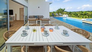 Un espacio al aire libre moderno con piscina, sillas de mimbre y una mesa blanca con tazas y tetera.