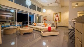 Uma sala moderna com sofá de canto, pufes e mesa de centro. Há uma janela grande que oferece vista para o exterior.