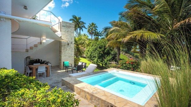 Uma área de piscina moderna ao ar livre, com um deck de pedra, uma mesa de madeira com cadeiras e uma escadaria que leva a um andar superior.