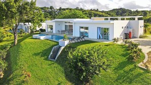 A modern house with a swimming pool, a patio, and a lush green lawn.