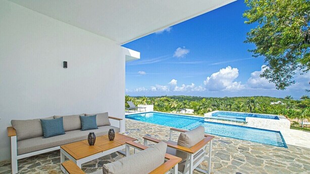 A modern outdoor seating area with a stone floor, a pool, and a view of a lush landscape.