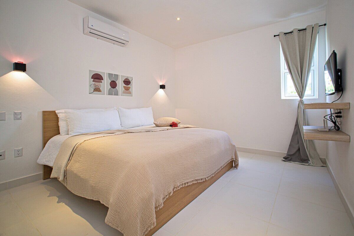 A bedroom with a bed, a TV, a shelf, and a window with curtains.