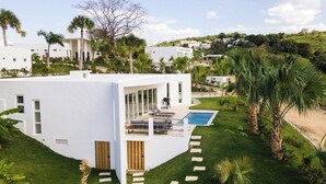 Un edificio blanco moderno con piscina, rodeado de palmeras y un césped cuidado.