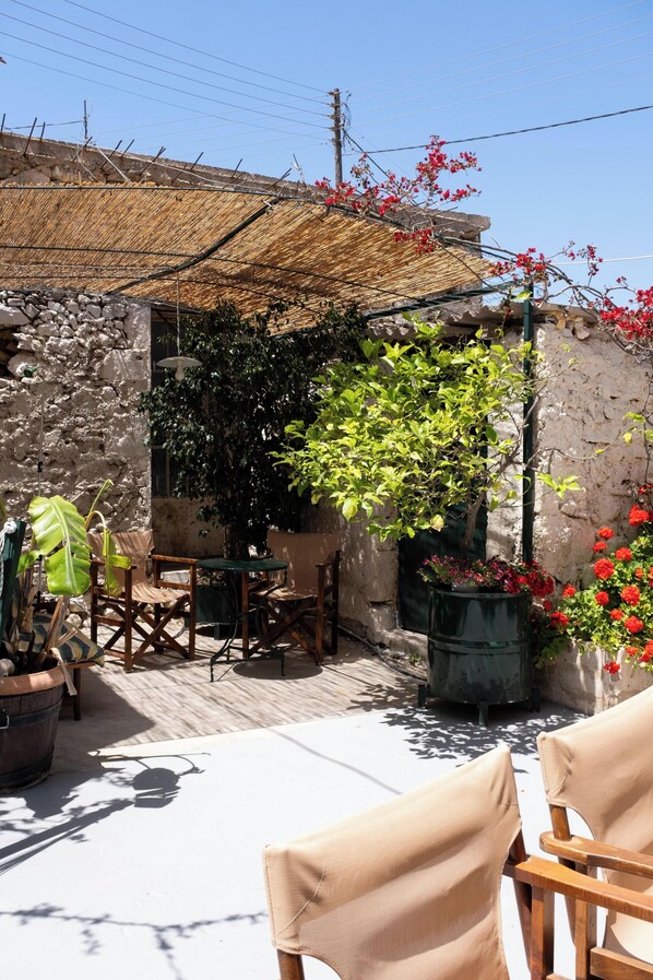 A patio area with outdoor seating, a stone wall, and a pergola with red flowers.