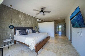 Une chambre avec un grand lit, un ventilateur de plafond, une télévision et une vue sur l’extérieur.