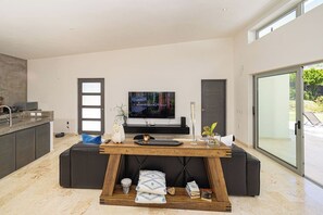 Een moderne woonruimte met een houten eettafel, zwarte leren banken, een flatscreen televisie en een keukenhoek.