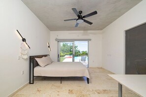 Un dormitorio con cama, ventilador de techo, puerta corrediza de vidrio a un patio y vista a una piscina.