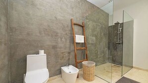 A bathroom with a toilet, bidet, wooden ladder, and a glass-enclosed shower area.