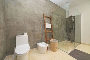 Une salle de bain comprenant des toilettes, un bidet, une échelle en bois et une douche séparée par une paroi de verre.