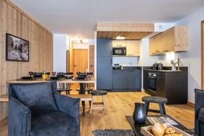 Eine moderne Küche mit Holzschränken, ein Essbereich mit Tisch für vier Personen und ein Wohnzimmer mit Sofa und Couchtisch.