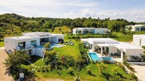 A modern resort with multiple white buildings, swimming pools, and lush green lawns.