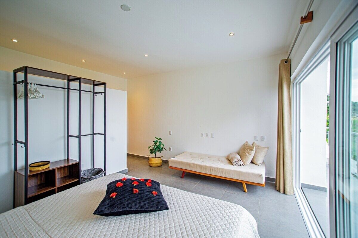 A modern bedroom with a large bed, a small sofa, a glass partition, and a view of the outdoors.