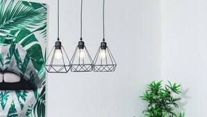 Un espace repas moderne avec une table en verre, trois suspensions et deux jardinières de couleur dorée contenant des plantes vertes.