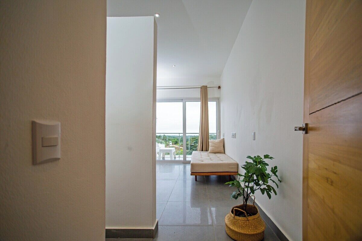 Una habitación de hotel moderna con balcón, una cama, una planta en maceta y una puerta de madera.