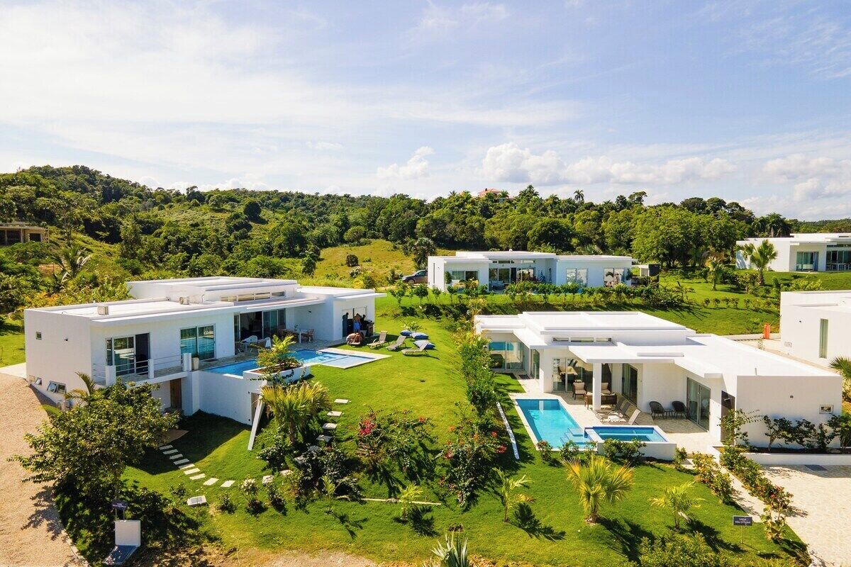 A modern resort with multiple white buildings, swimming pools, and lush green lawns.