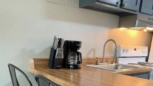 A kitchen with a wooden countertop, two bar stools, a coffee maker, and a sink. - Cute Condo with Pool (Huddleston)
