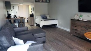 A modern living room with a sofa, a bed, a TV, and a dining area. - Cute Condo with Pool (Huddleston)