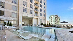 Ett modernt poolområde på hotellet med solstolar, en vattenrutschkana och utsikt över en hög byggnad.