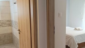 Une chambre d’hôtel avec une porte en bois, un lit avec du linge de lit blanc et un luminaire suspendu.