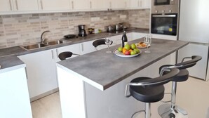 Une cuisine moderne avec des meubles blancs, un plan de travail gris et un îlot central doté de tabourets de bar.