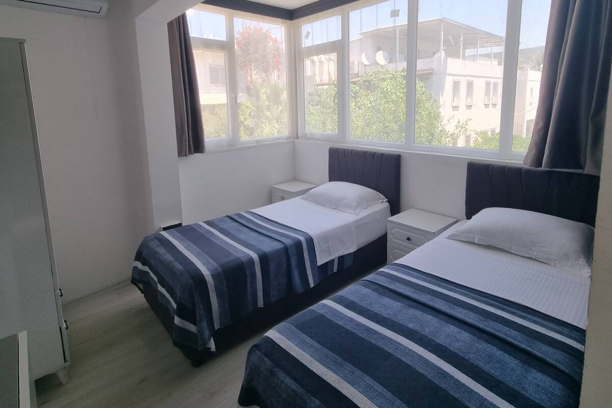 A bedroom with two beds, a window with curtains, an air conditioning unit, and a ceiling fan.