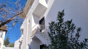 A modern white building with a balcony, a door, and a small garden area with plants. - Kardelen Otel (Bodrum)