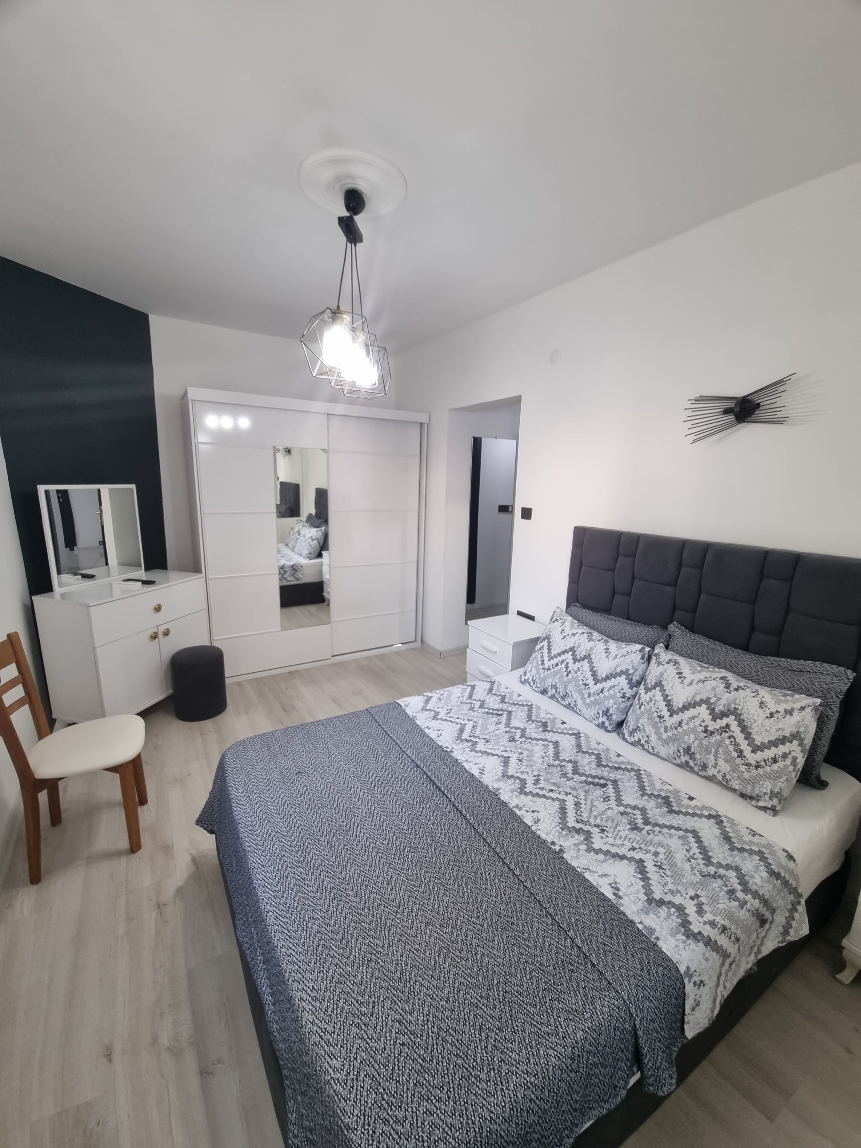 Un dormitorio con cama, cómoda, espejo y lámpara colgante.