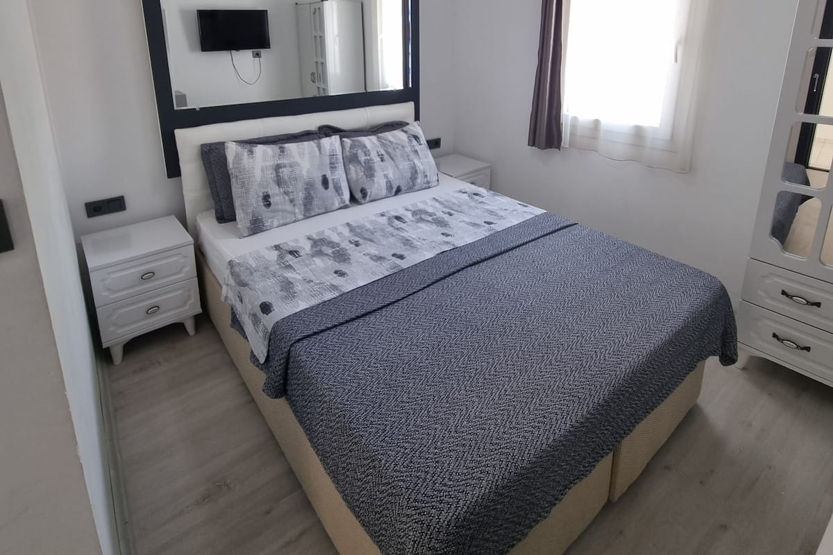 A modern bedroom with a bed, bedside tables, a mirror, and a window with curtains.