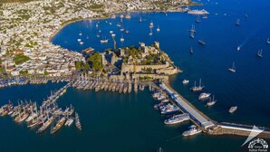 An aerial view of a coastal town with a historic castle, a marina with numerous boats, and a densely packed residential area. - Kardelen Otel (Bodrum)