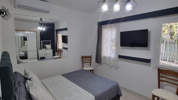 A bedroom with a bed, a desk, a chair, a TV, a mirror, and a ceiling fan. - Kardelen Otel (Bodrum)